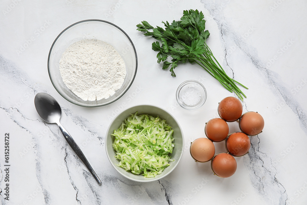 Bowls with grated zucchini, flour and eggs for preparing fritters on white marble background