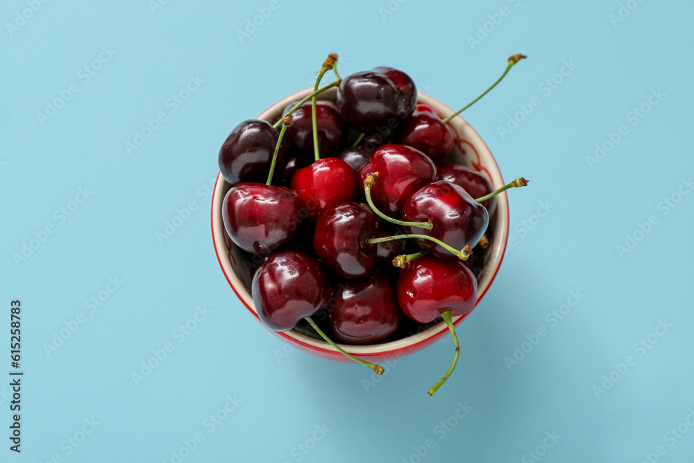 Bowl with sweet cherries on blue background