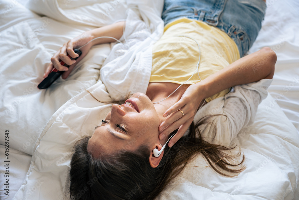 Caucasian young woman listen to music while lying down on bed in house. 