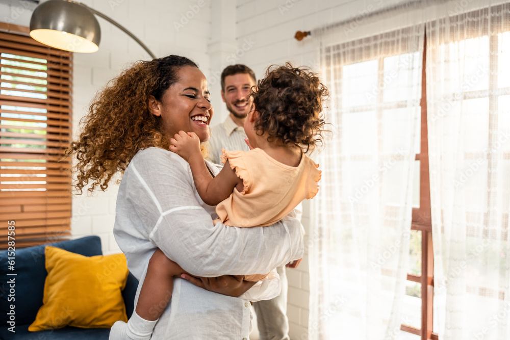 African American mother tosses young baby girl up in living room at home. 