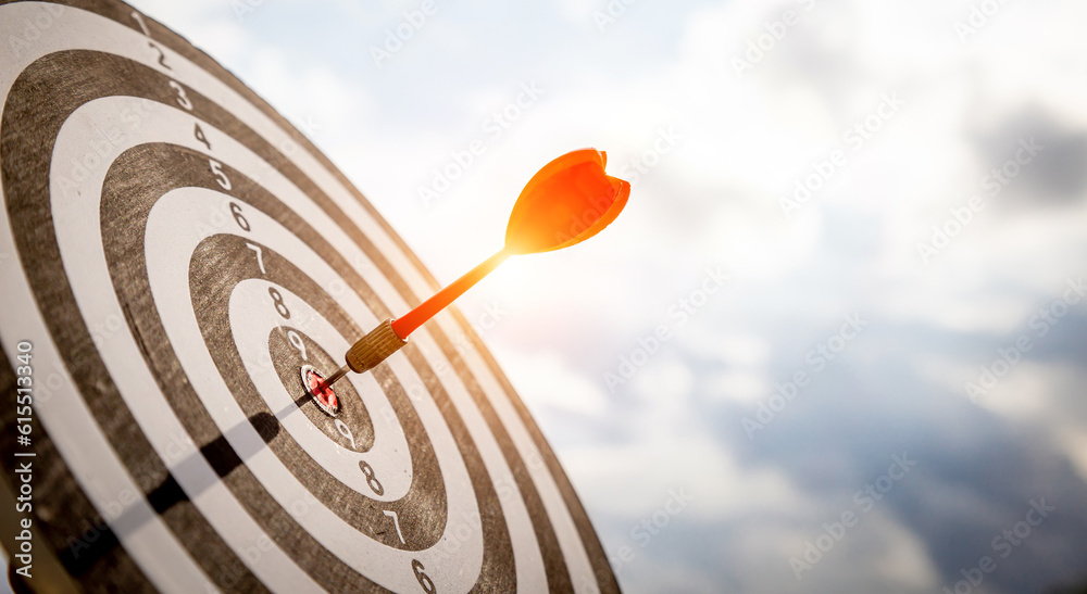 Close up shot red darts arrows in the target  of dartboard center on dark blue sky background. Busin