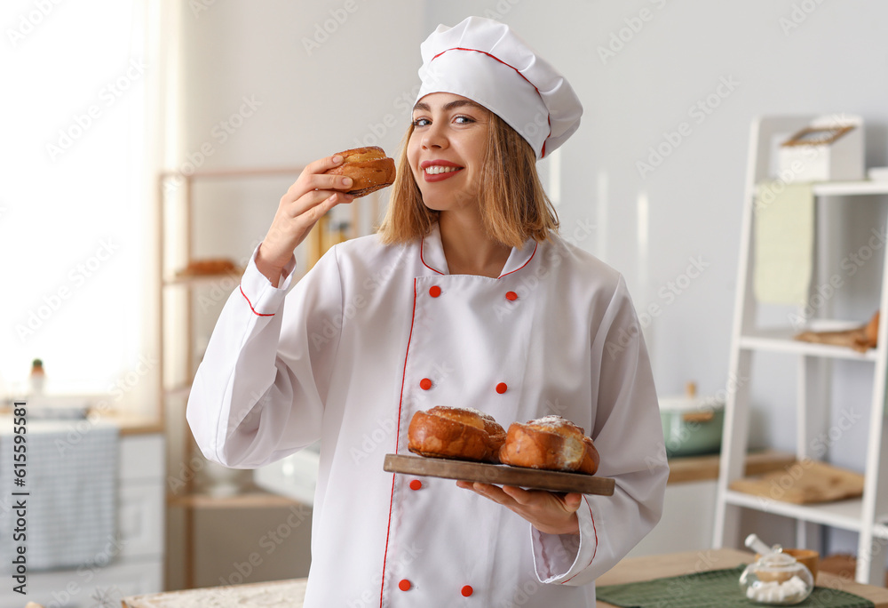 Female baker with board of tasty buns in kitchen