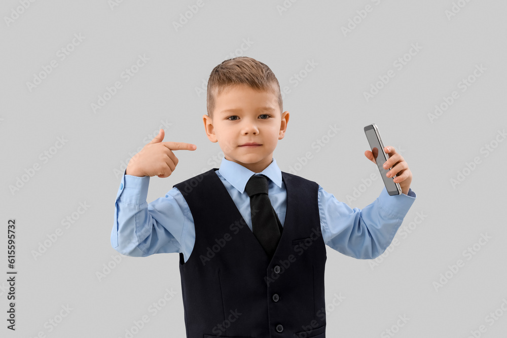 Cute little businessman pointing at mobile phone on grey background