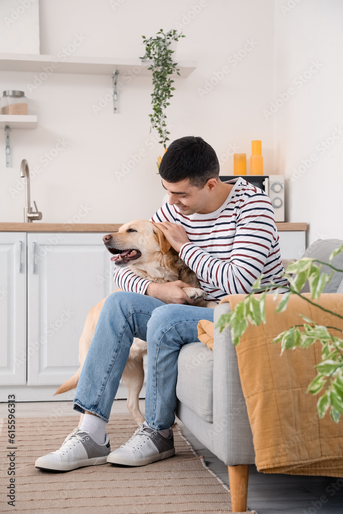 Young man with cute Labrador dog sitting in kitchen