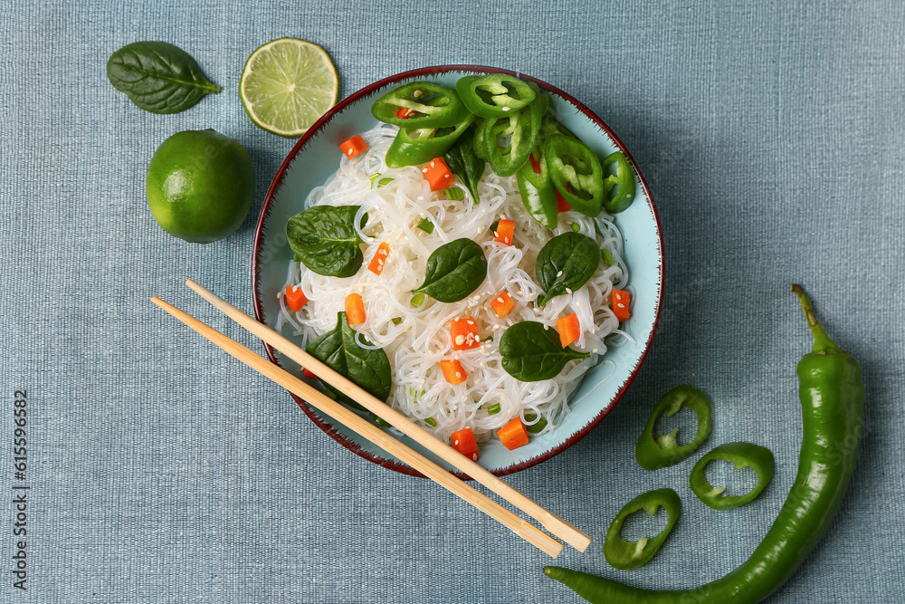 Composition with bowl of tasty rice noodles, chili pepper and lime on color fabric background