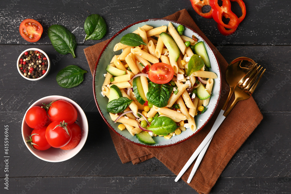 Bowl with tasty pasta salad and ingredients on dark wooden background