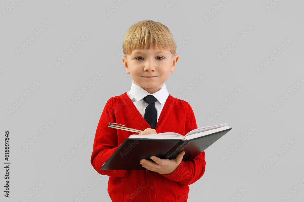 Funny little businessman writing in notebook on grey background