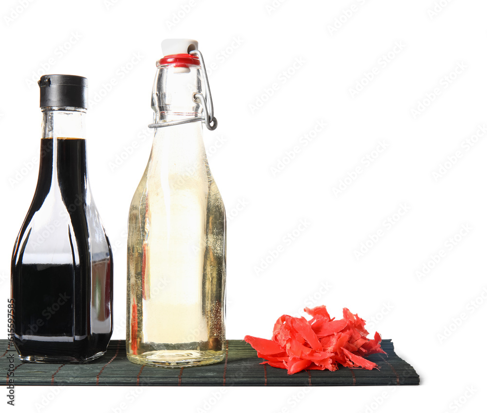 Bottles of rice vinegar, soy sauce, ginger and bamboo mat on white background