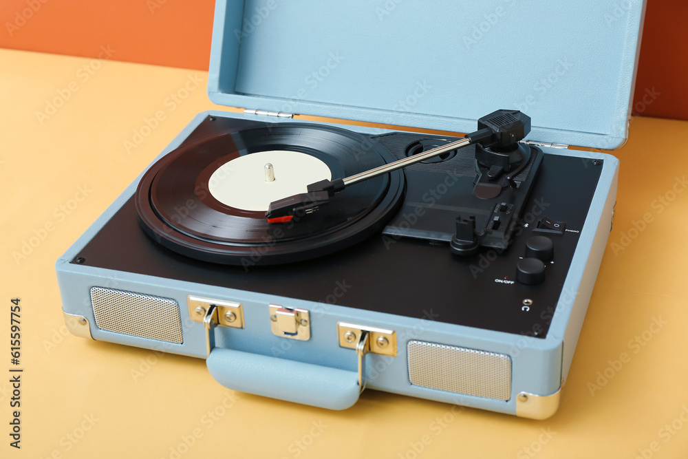 Record player with vinyl disk on table near orange wall