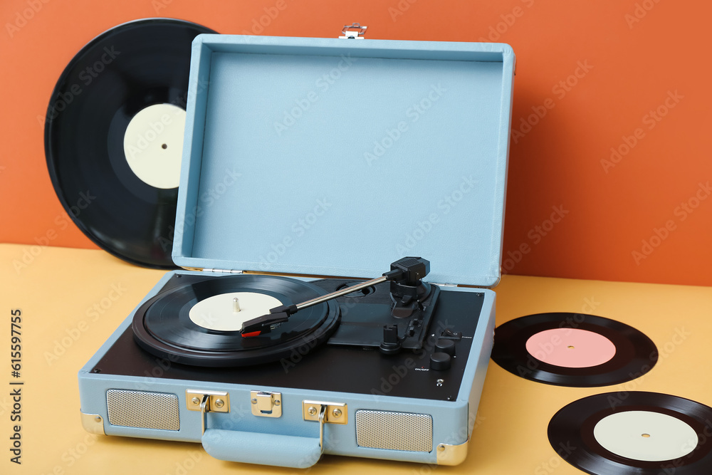 Record player with vinyl disks on table near orange wall