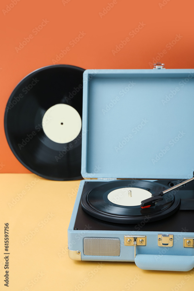 Record player with vinyl disks on table near orange wall