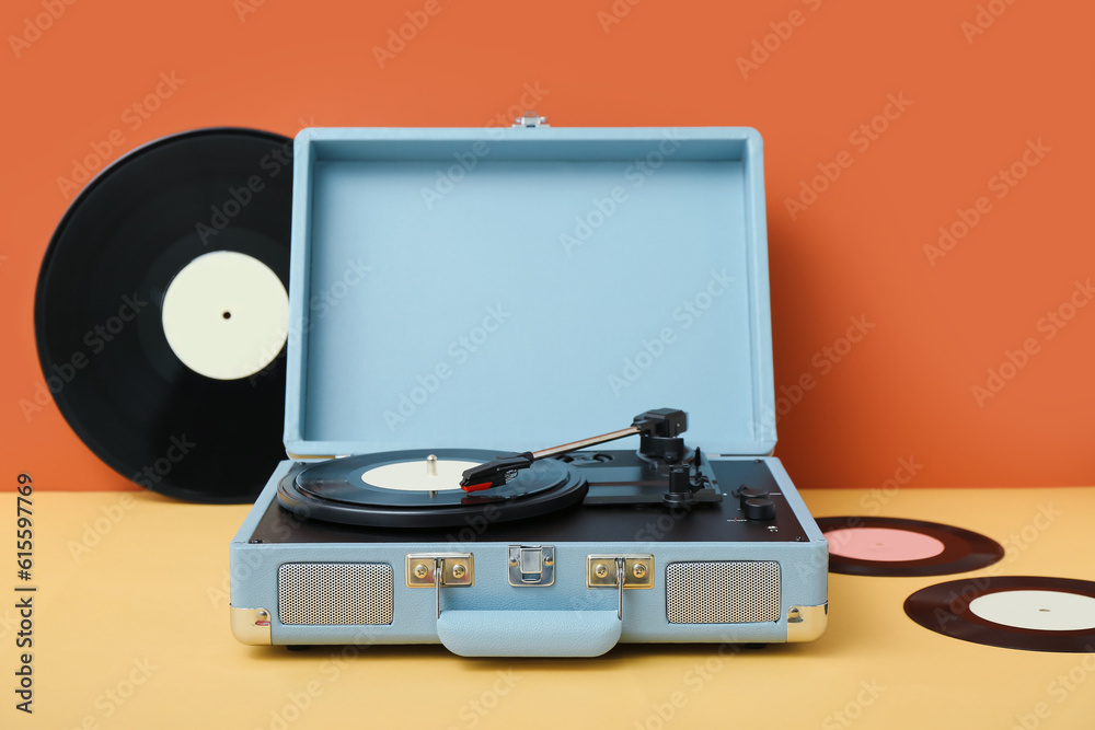 Record player with vinyl disks on table near orange wall