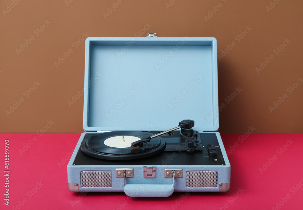 Record player with vinyl disk on table near brown wall