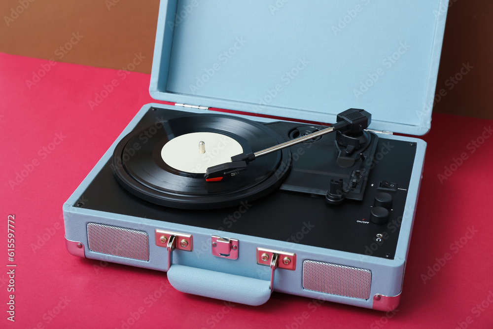 Record player with vinyl disk on table near brown wall