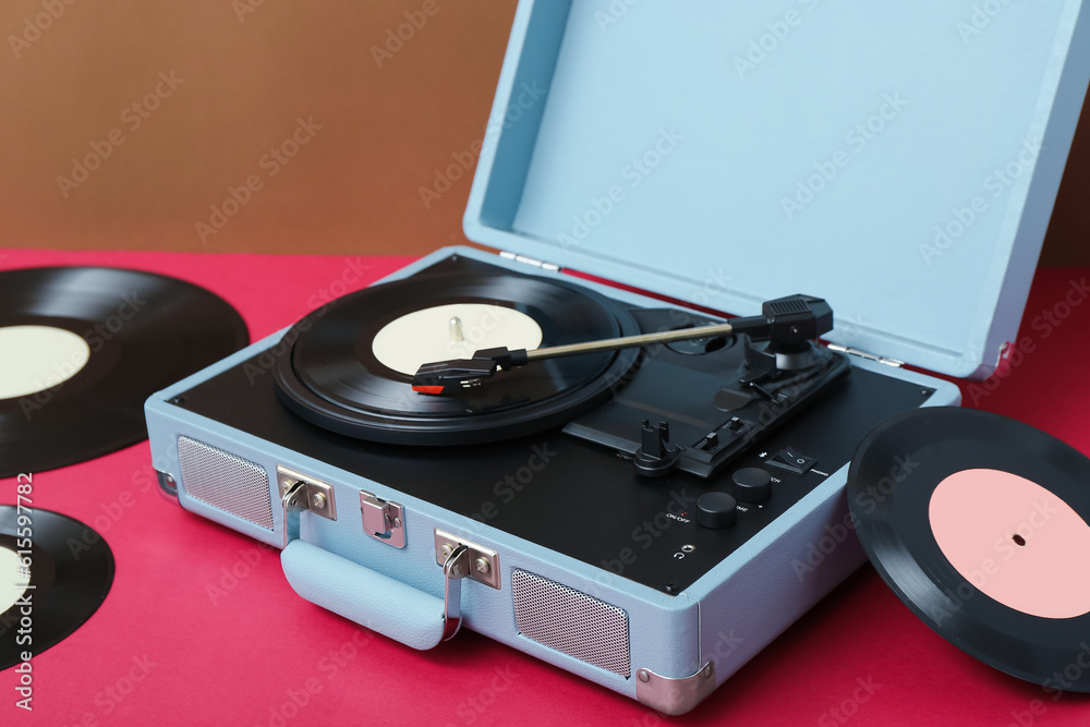 Record player with vinyl disks on table near brown wall