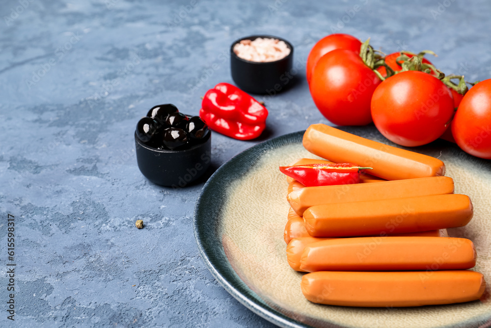 Plate with sausages, tomatoes and olives on blue background