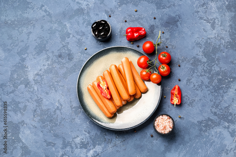 Plate with sausages, tomatoes and olives on blue background