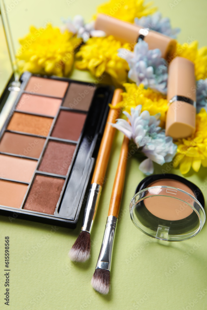 Eyeshadows with lipsticks, brushes and flowers on green background, closeup