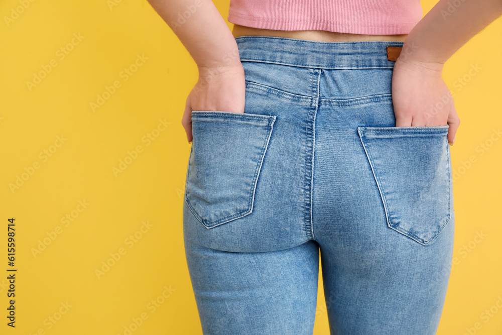 Young woman in stylish jeans on yellow background, back view