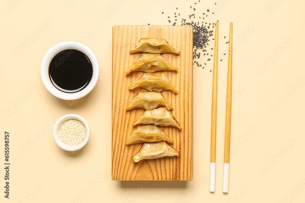 Wooden board with tasty Chinese jiaozi, sesame and sauce on beige background