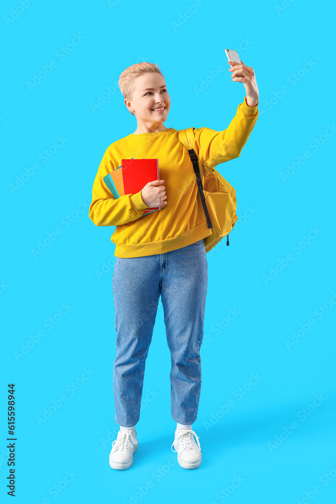 Female student with notebooks taking selfie on blue background