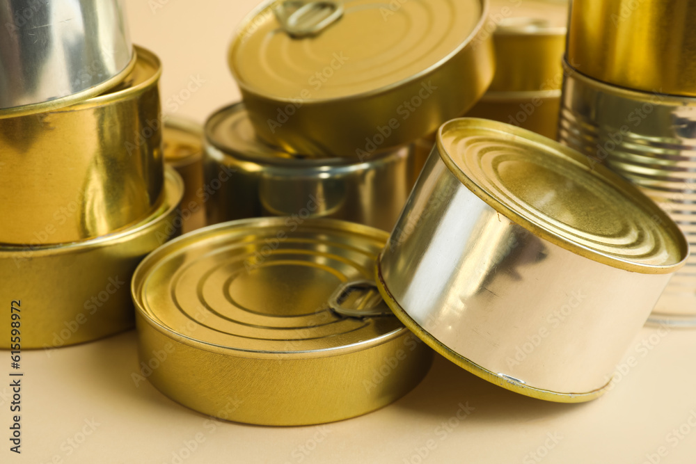 Different tin cans with fish on beige background, closeup