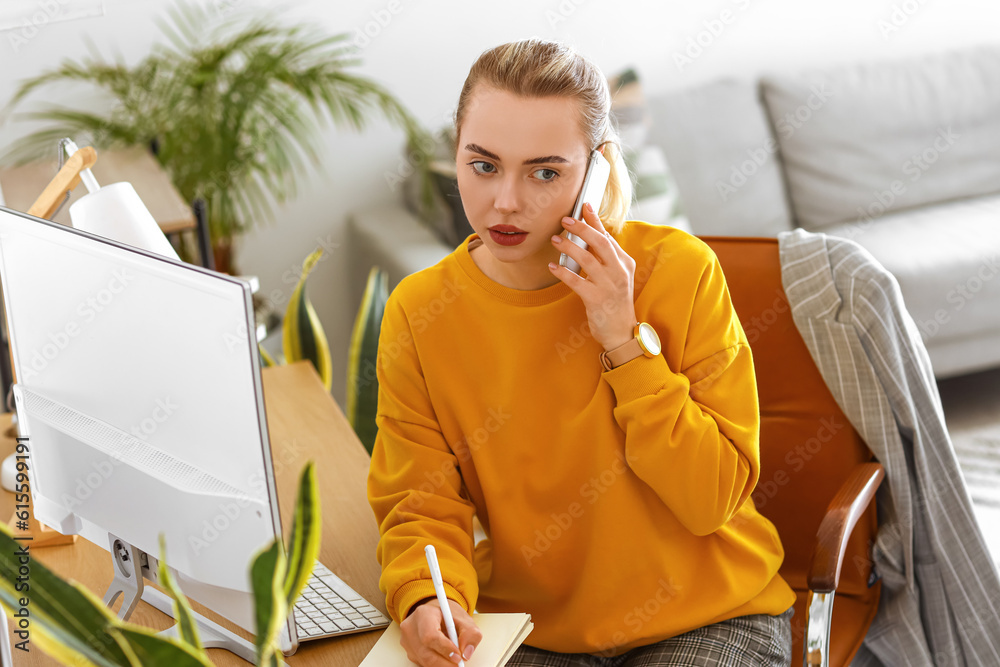 Female student with notebook talking by mobile phone at home