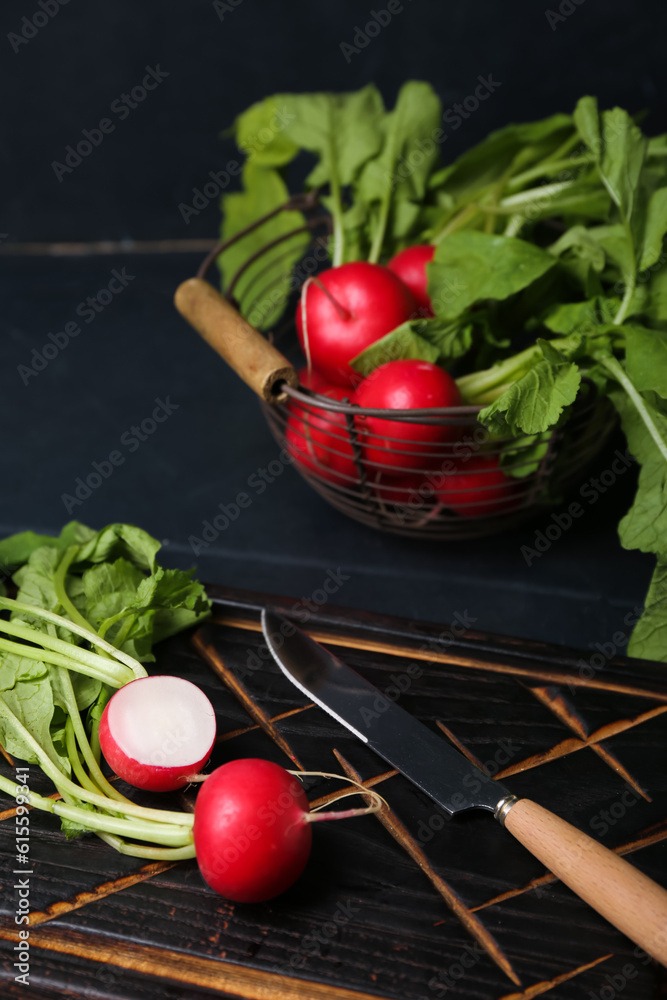 Wooden board and basket of ripe radish with green leaves on dark background