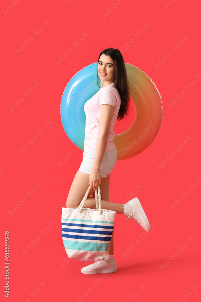 Young woman with inflatable ring and beach bag on red background