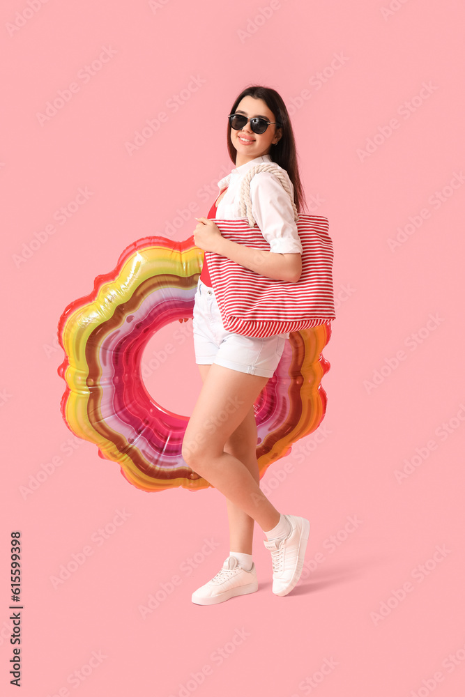 Young woman with inflatable ring and beach bag on pink background