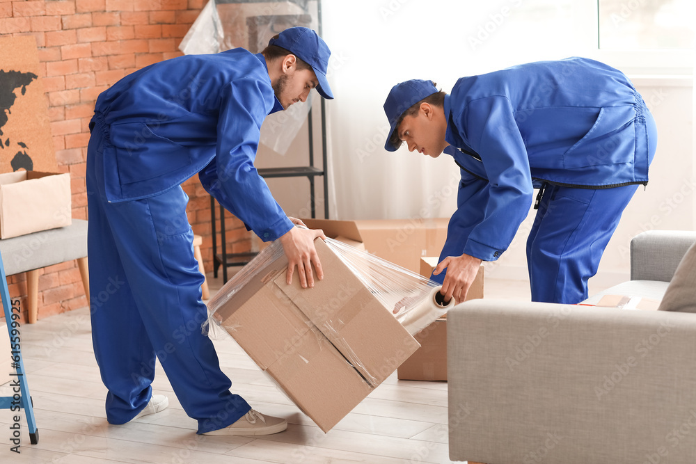 Male movers wrapping box with stretch film in room