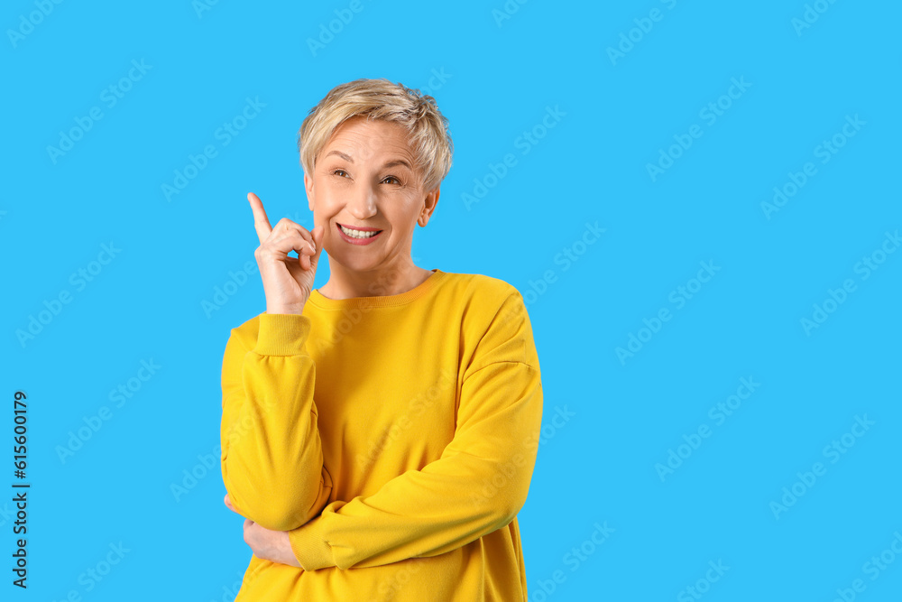 Dreaming mature woman pointing at something on blue background