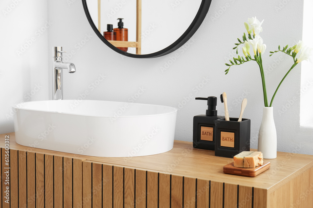 White sink, bath accessories and vase with flowers on table in room