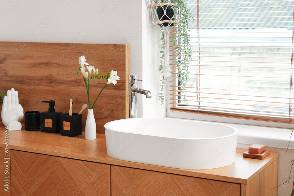 Sink, bath accessories and vase with flowers on table in room