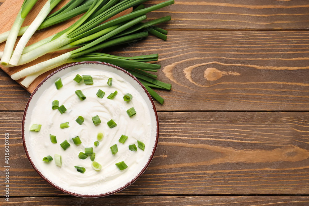 Bowl of tasty sour cream with green onion on wooden background