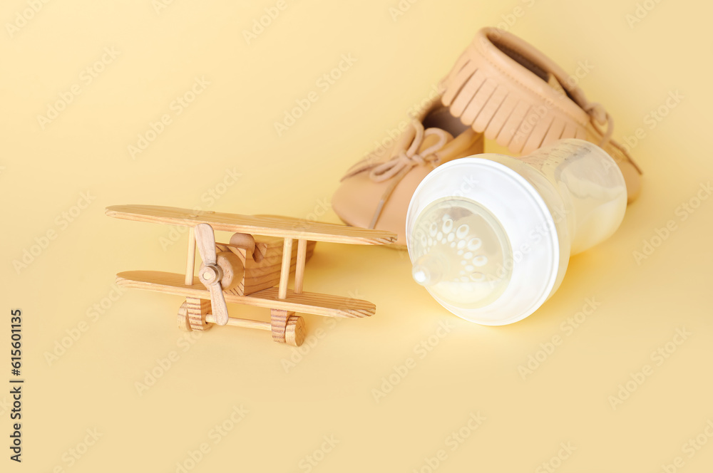 Bottle of milk for baby with toy and booties on pale yellow background