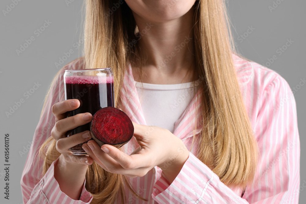 Young woman with glass of vegetable juice and beet on grey background, closeup