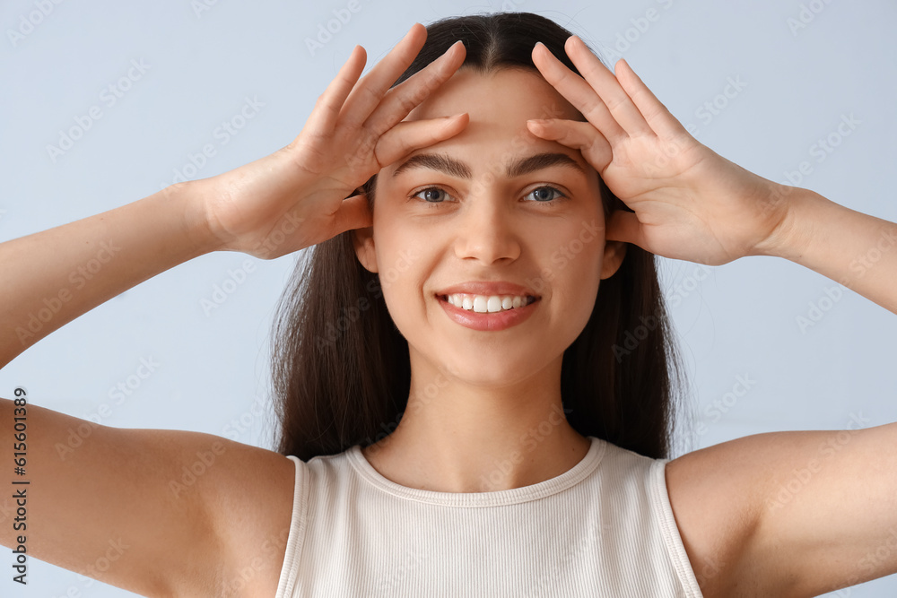 Young woman doing face building exercise on light background, closeup