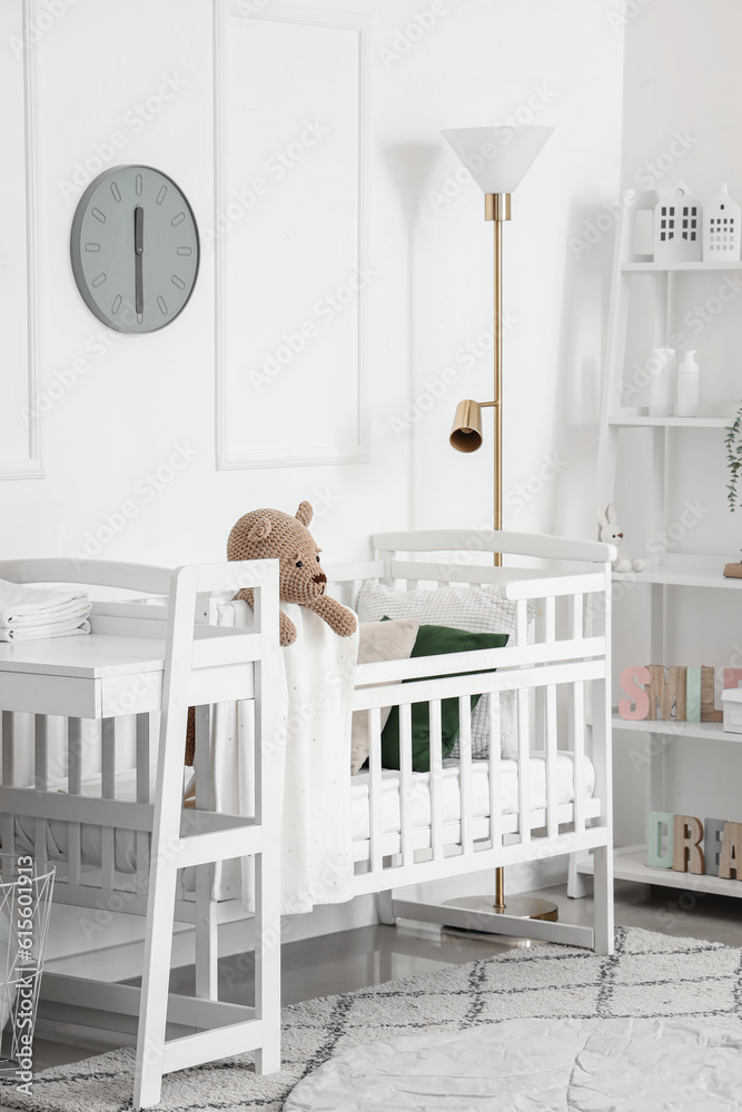 Interior of light bedroom with baby crib, changing table and shelving unit