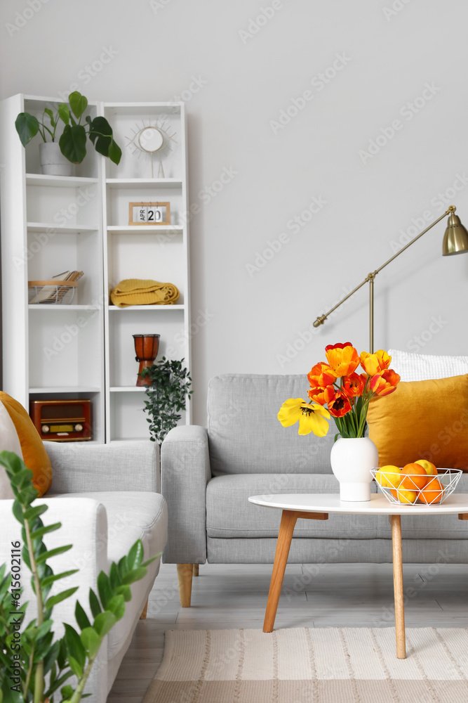 Interior of stylish living room with cozy sofas and tulip flowers on coffee table