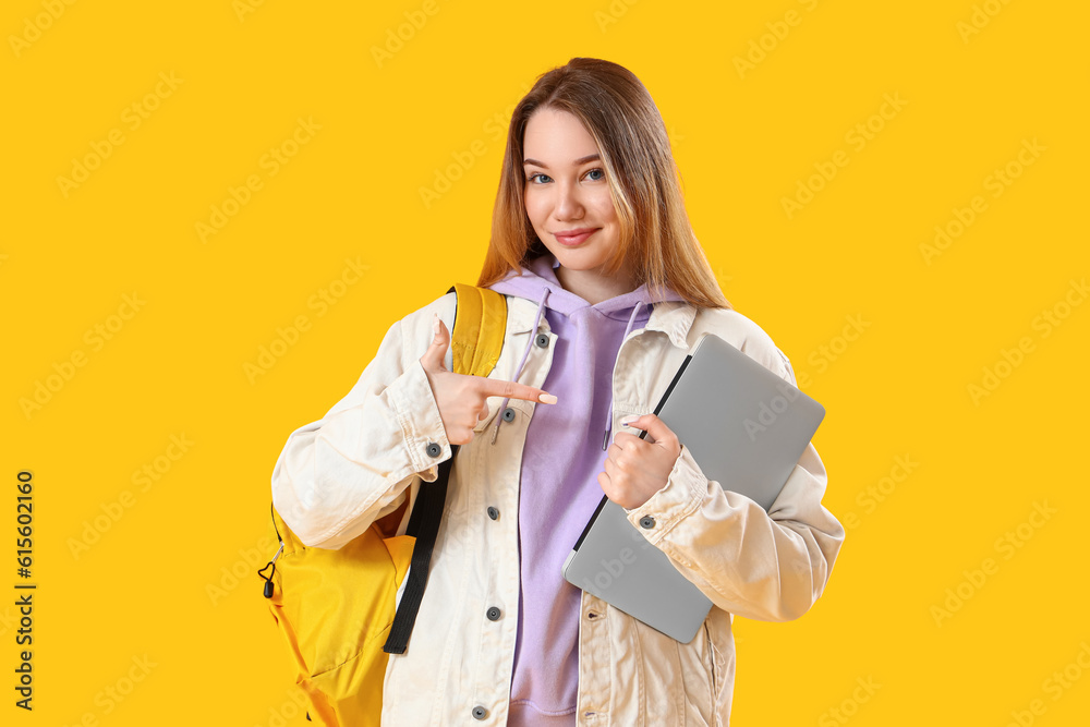 Female student pointing at laptop on yellow background