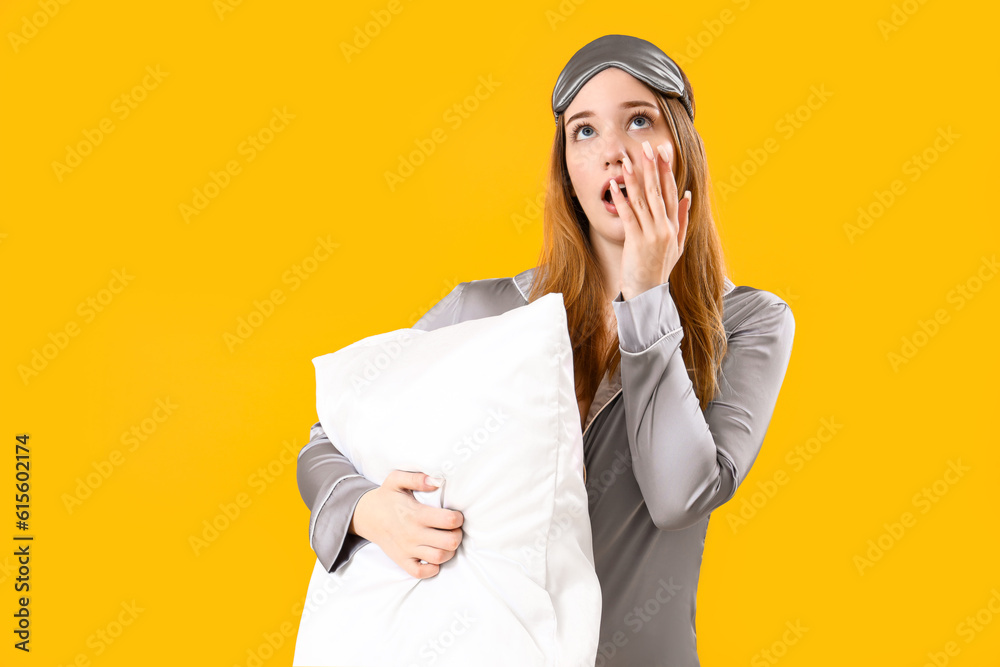 Young woman in pajamas with pillow on yellow background