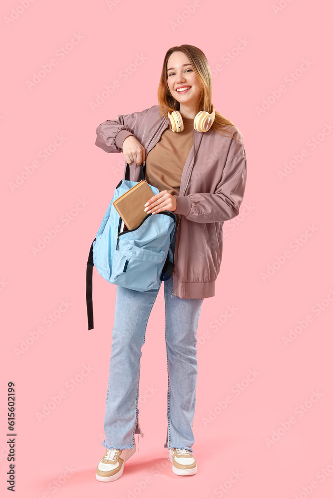 Female student putting book into backpack on pink background