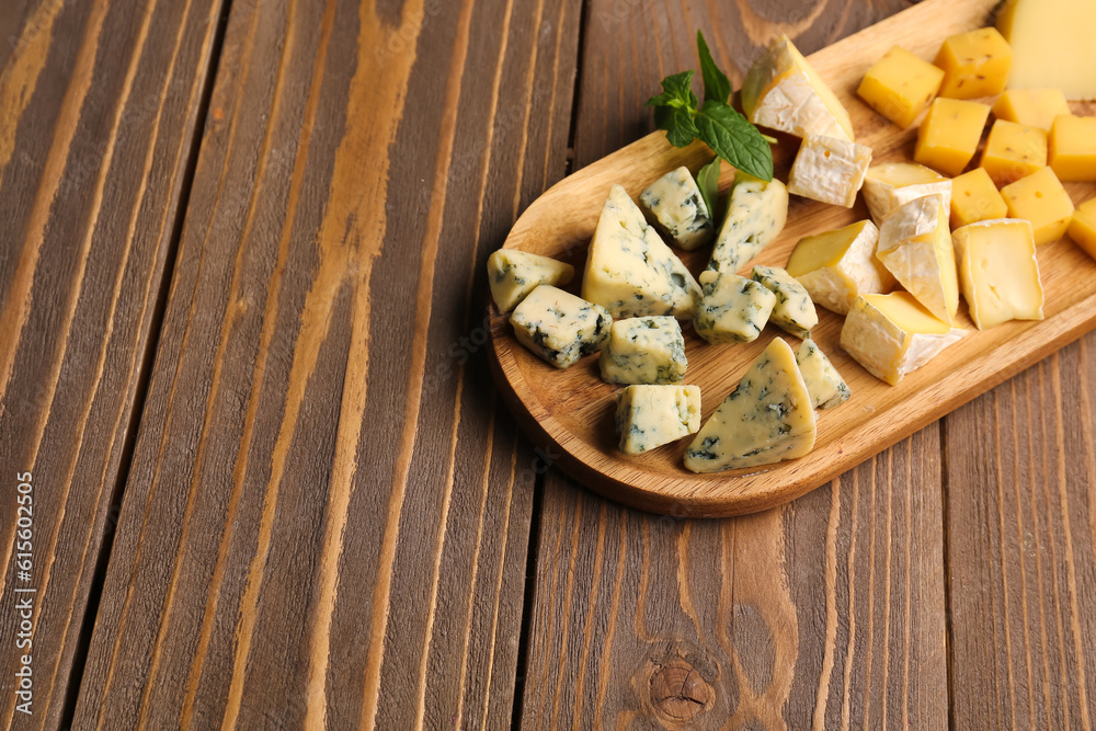 Board with pieces of tasty cheese on wooden background, closeup