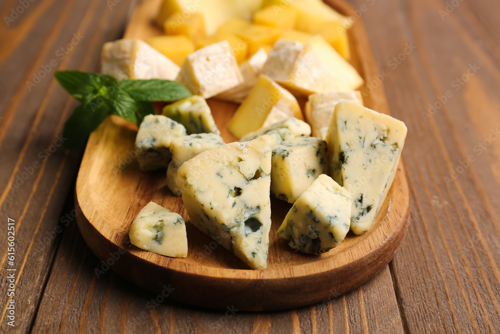 Board with pieces of tasty cheese on wooden background, closeup