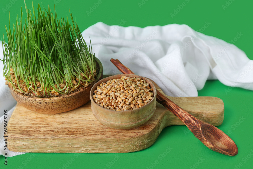 Bowl with fresh wheatgrass and wooden board on green background