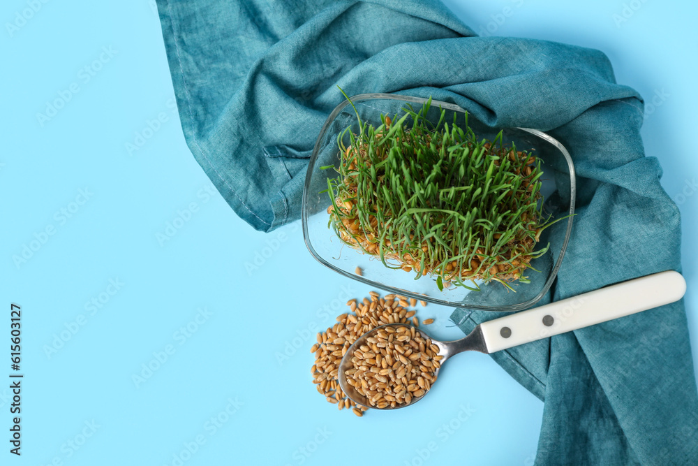 Bowl with fresh wheatgrass, spoon and kitchen towel on blue background