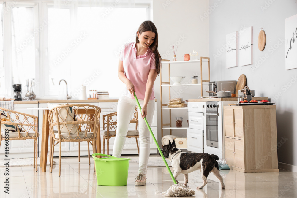 Young woman with her French bulldog mopping floor in kitchen