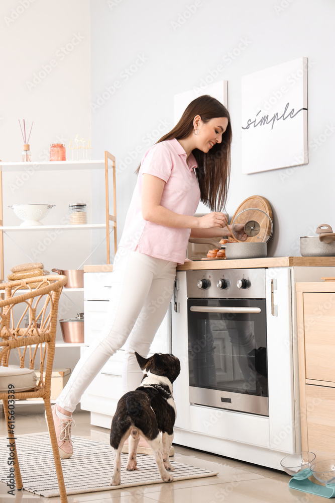 Young woman with her French bulldog cooking in kitchen