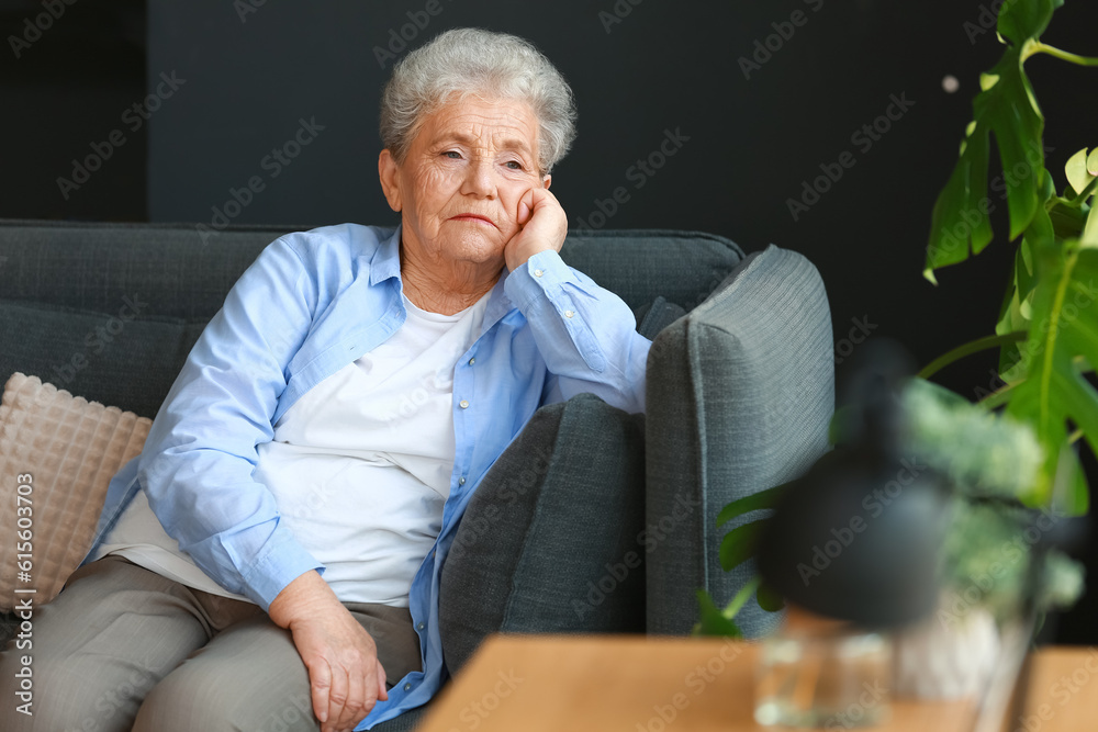 Sad senior woman sitting on sofa at home